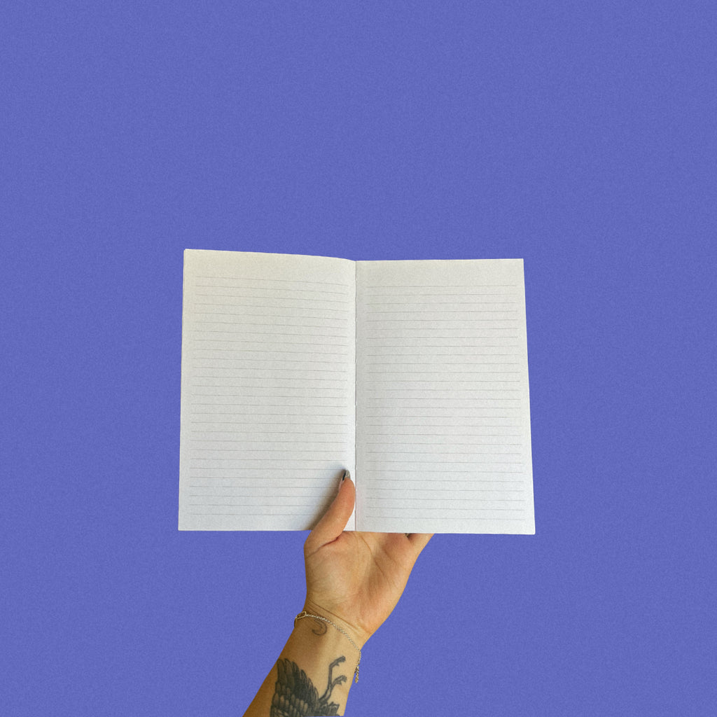 Hand holding an open notebook with lined pages against a blue background